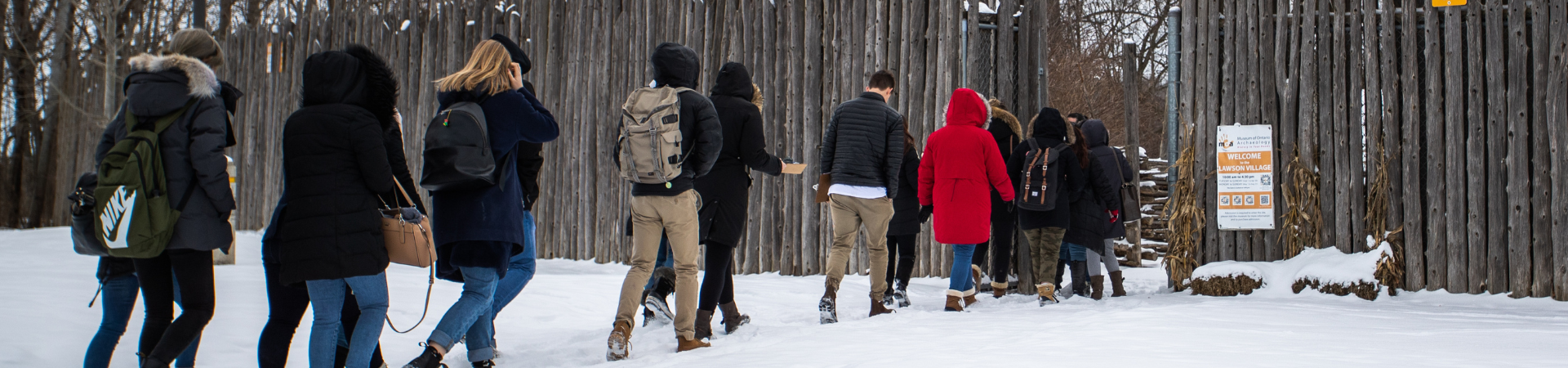 Several people walk in a line to enter a wooded area.