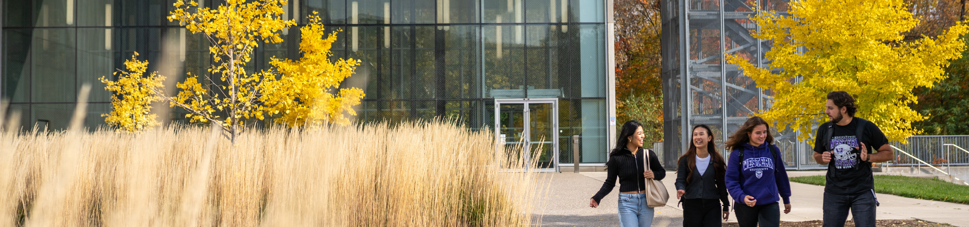 Two men stand outside, with one pointing to something in the distance.