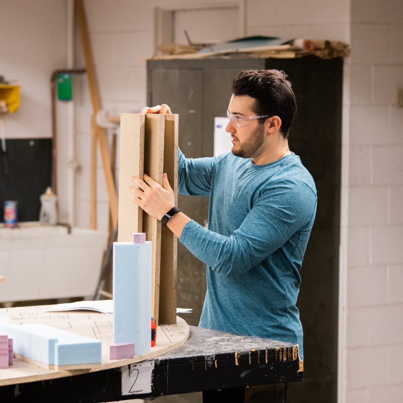 A young man works on a model building made of styrofoam.