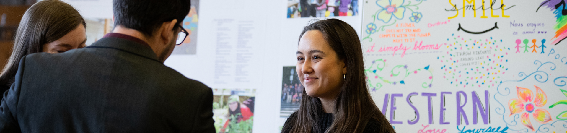 A smiling young woman stands in front of a poster board.