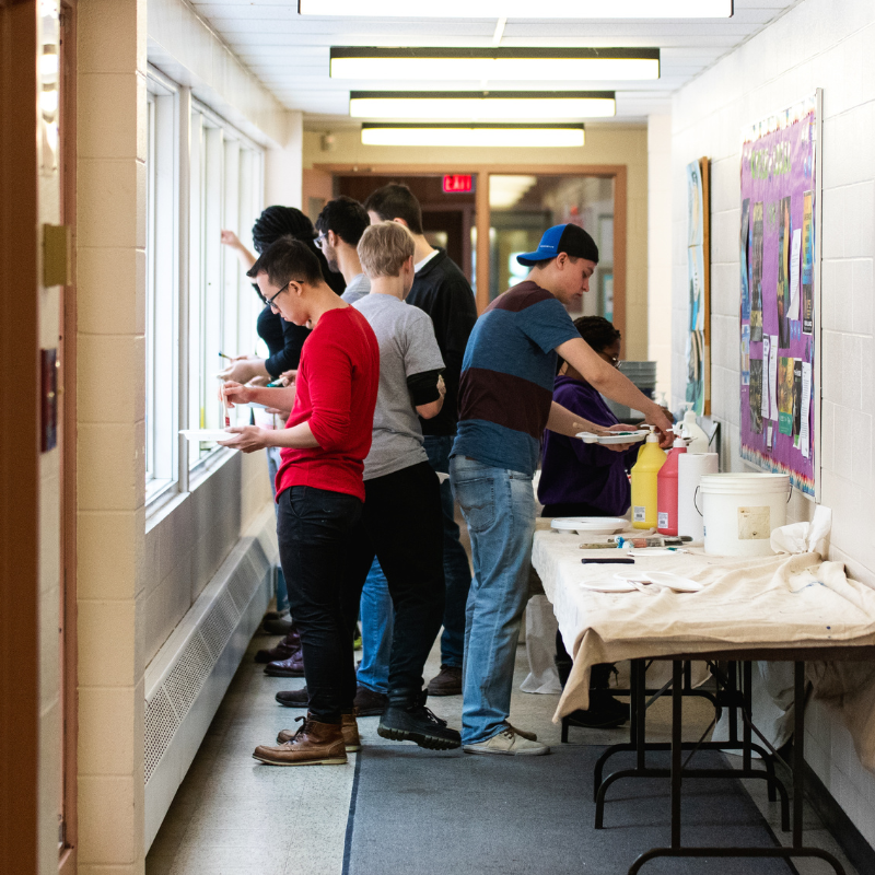 Several students stand in a hallway working on a project.